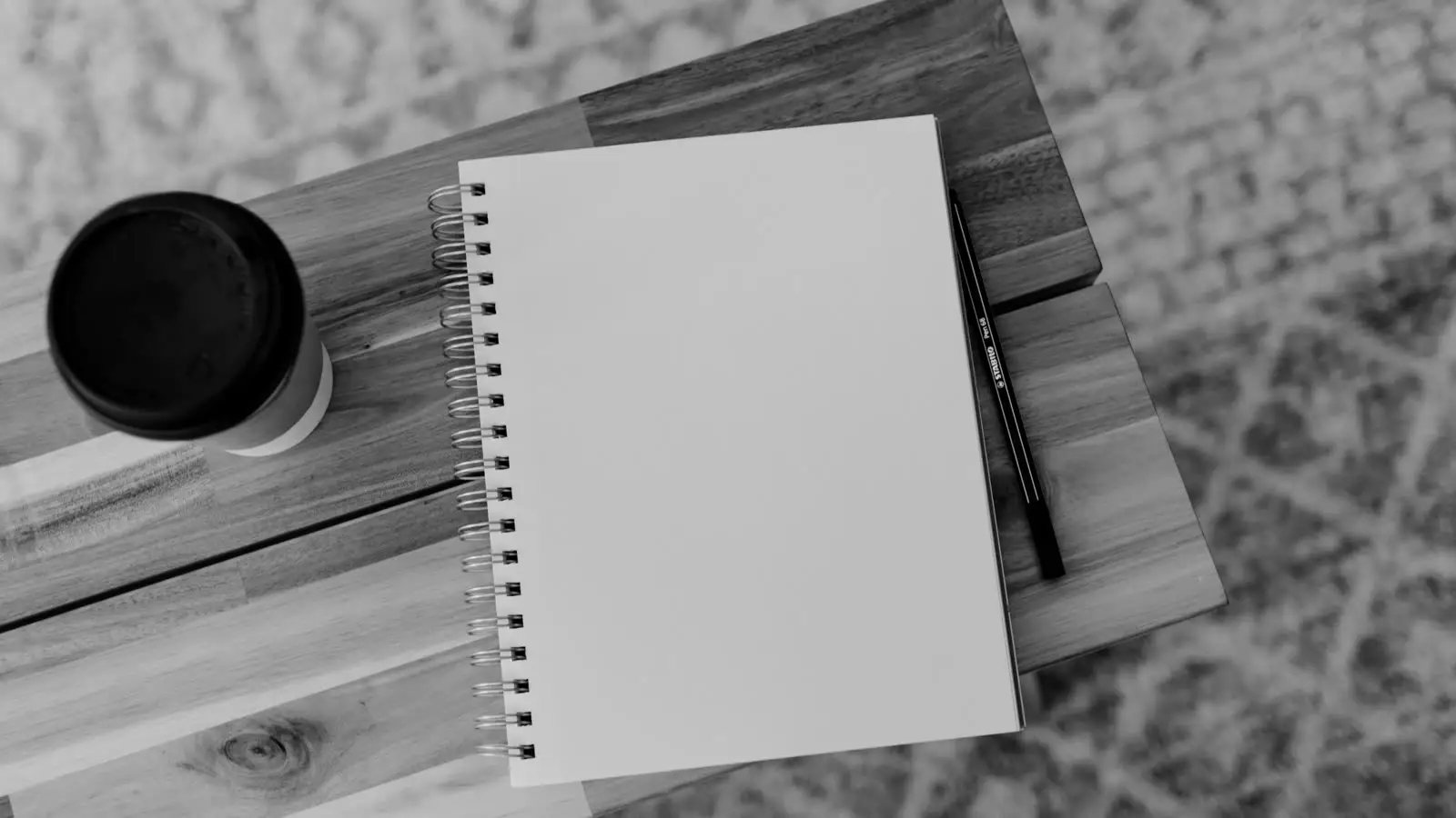 Ahşap masa üzerinde boş bir defter, kalem ve kahve